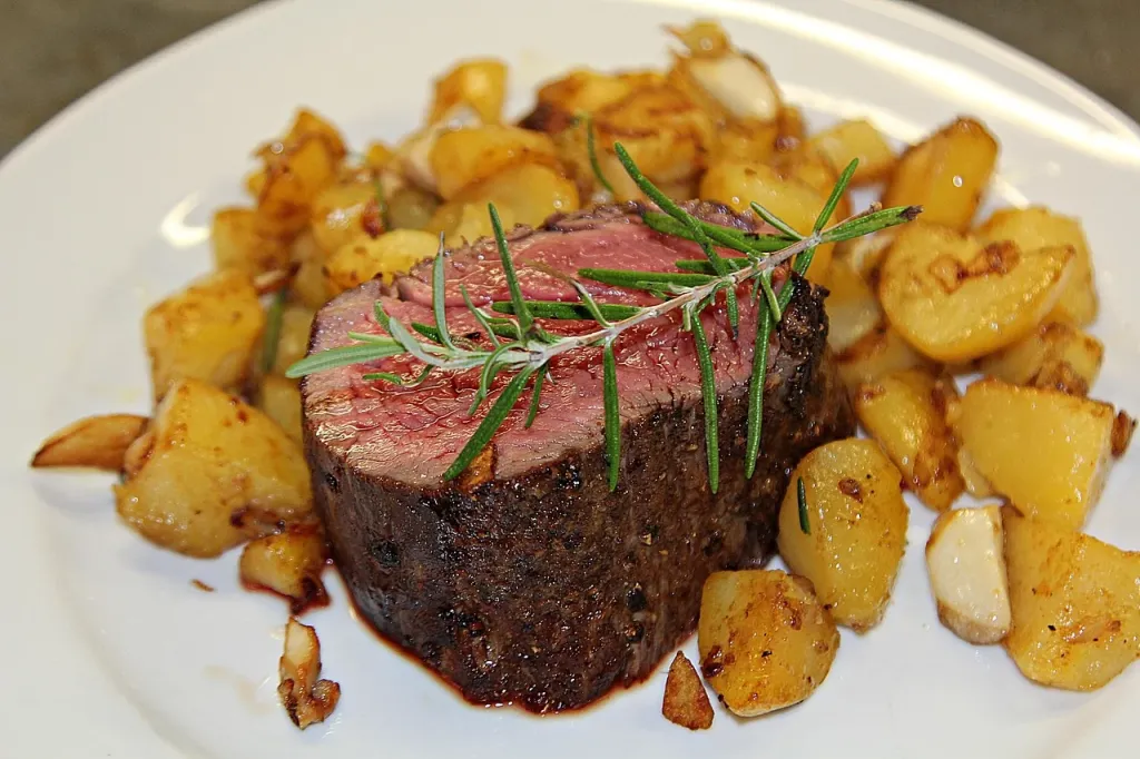 Soczysty stek ribeye medium-rare pokrojony w plastry, podany z masłem ziołowym i rozmarynem na rustykalnym talerzu.
